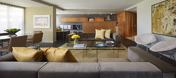 This open concept living room, furnished with mid-century modern classics, is backed by an open kitchen with cement panels